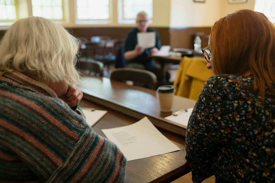 An older woman and a younger woman sitting side by side at a table, reading papers together