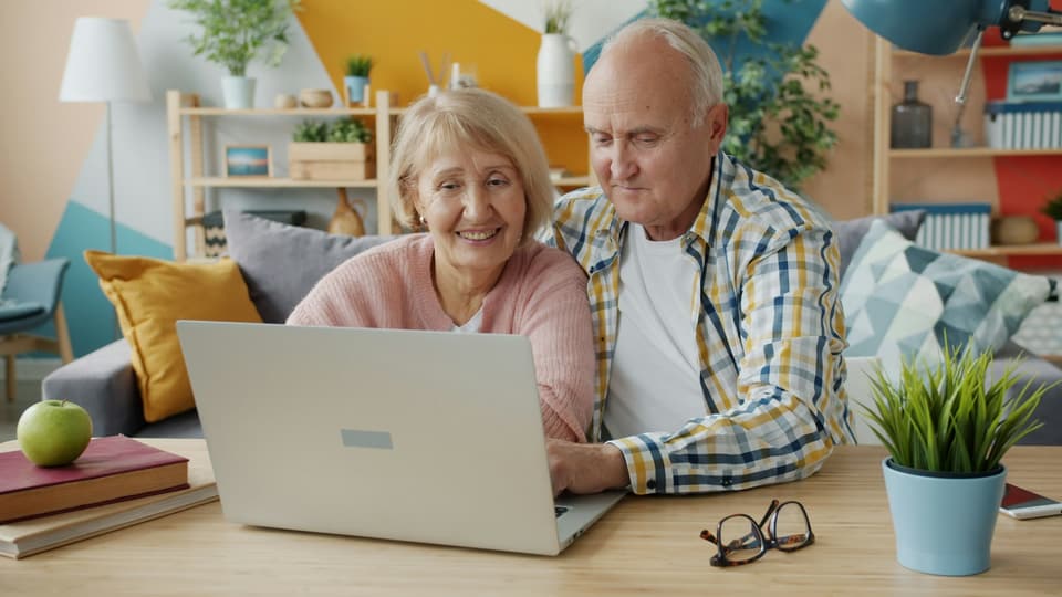 An older couple smiling at a laptop together at home