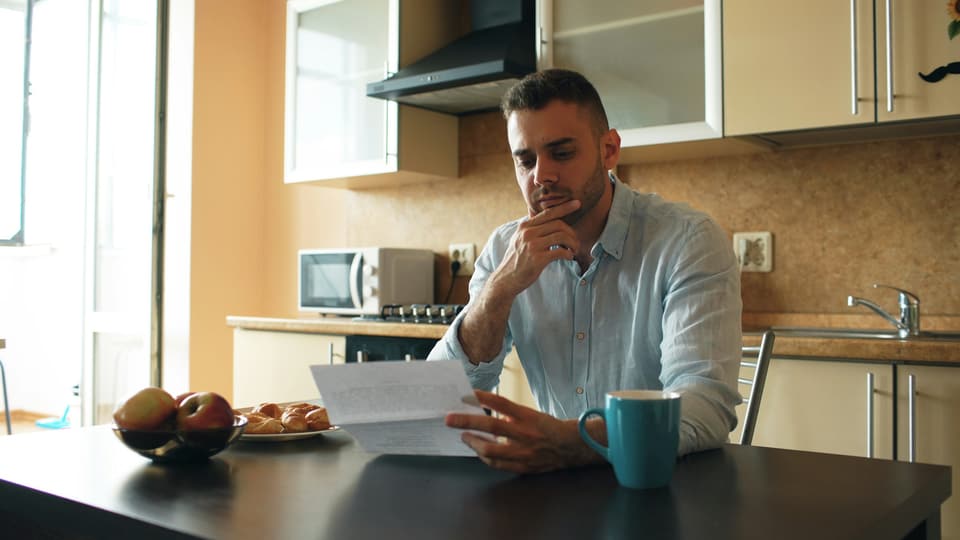 A man reading a letter at his kitchen table, a mug of coffee beside him
